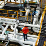 A MEP worker wearing an orange shirt stands confidently on a pipe, showcasing his expertise and dedication to his job.